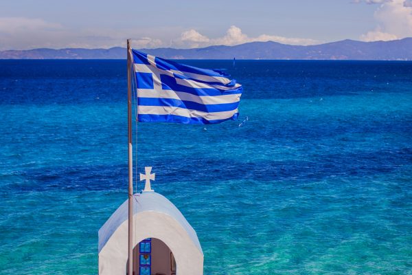 The Greek National Flag over seascape, beautiful turquoise sea , summer travel vacation destination.